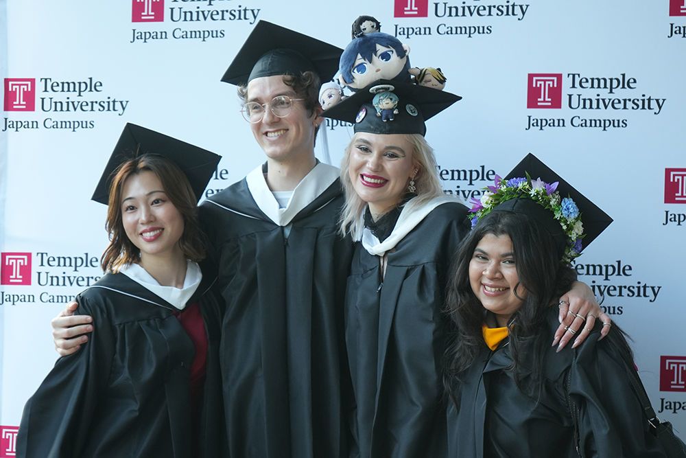 Graduates taking a picture in front of the backdrop at Hitomi Hall