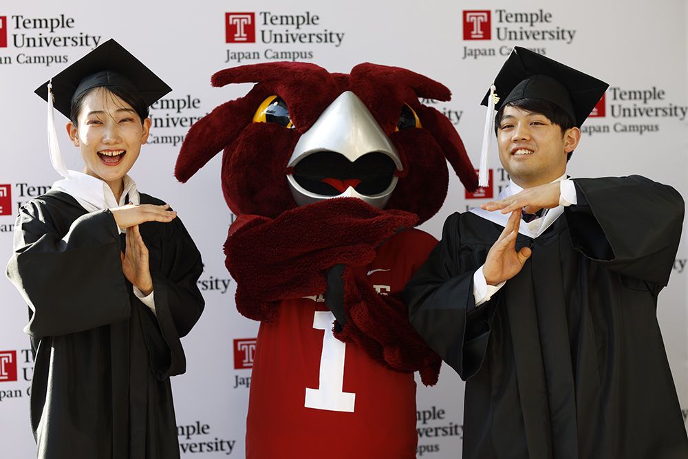 Graduates taking a picture in front of the backdrop at Hitomi Hall