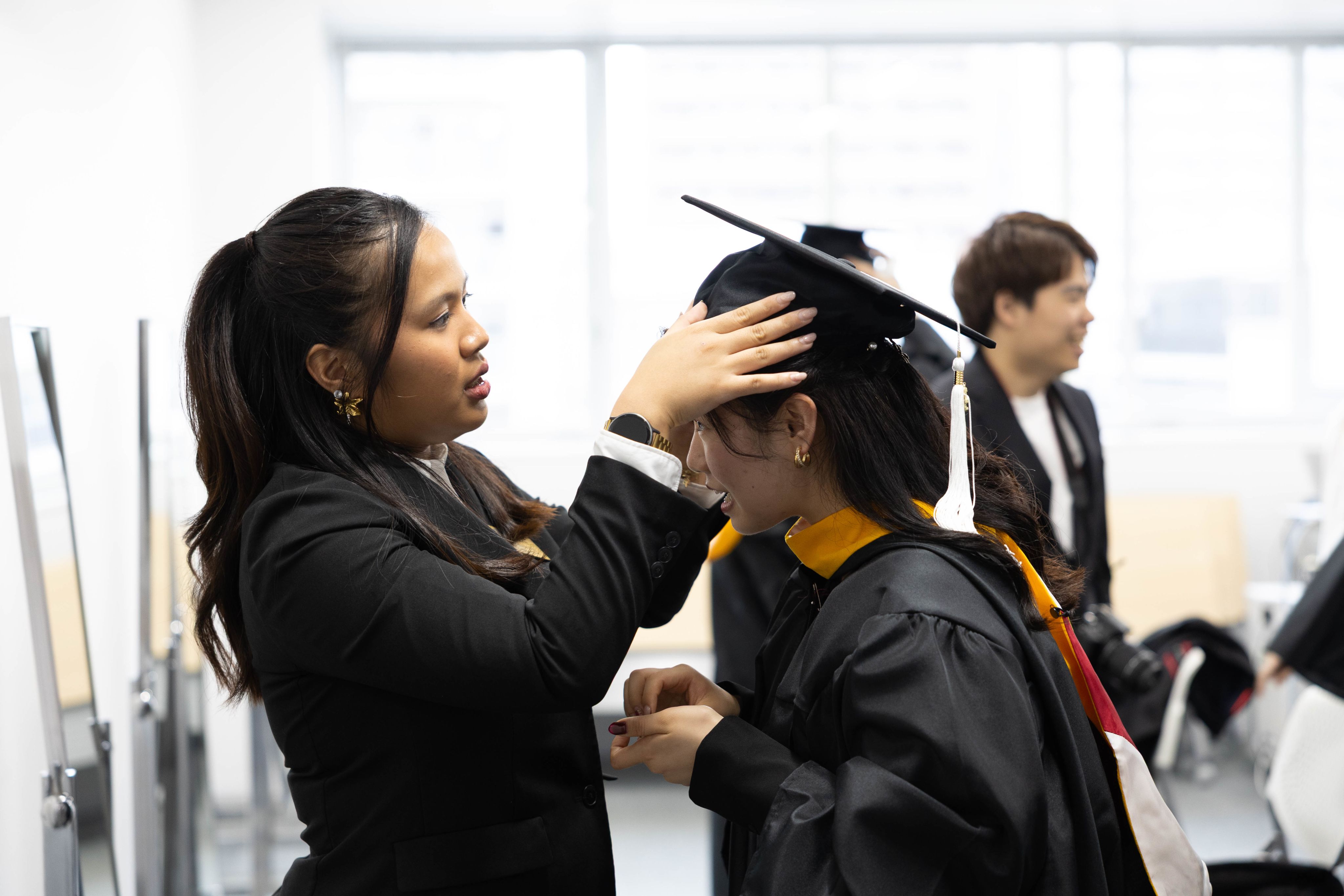  A graduate robing for the commencement, assisted by a staff member.