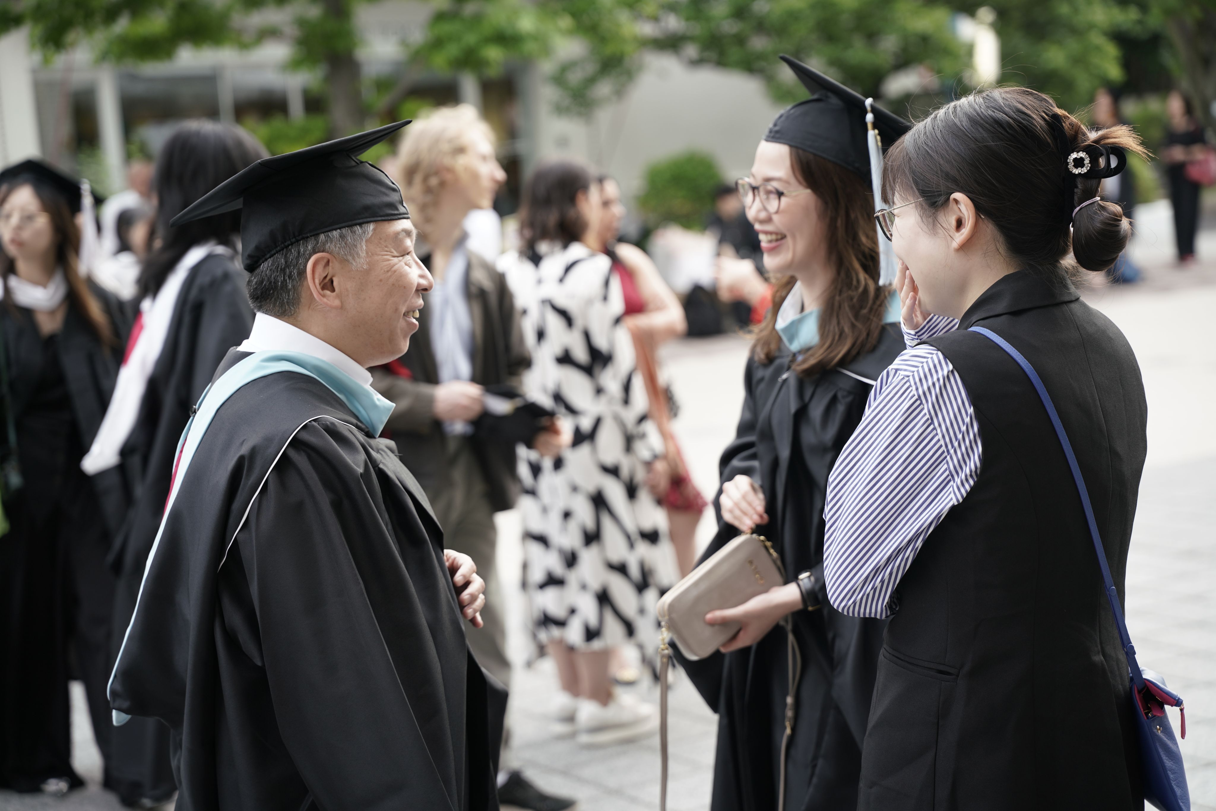 A group of graduates conversing in front of Hitomi Hall, capturing the joy of their commencement ceremony.
