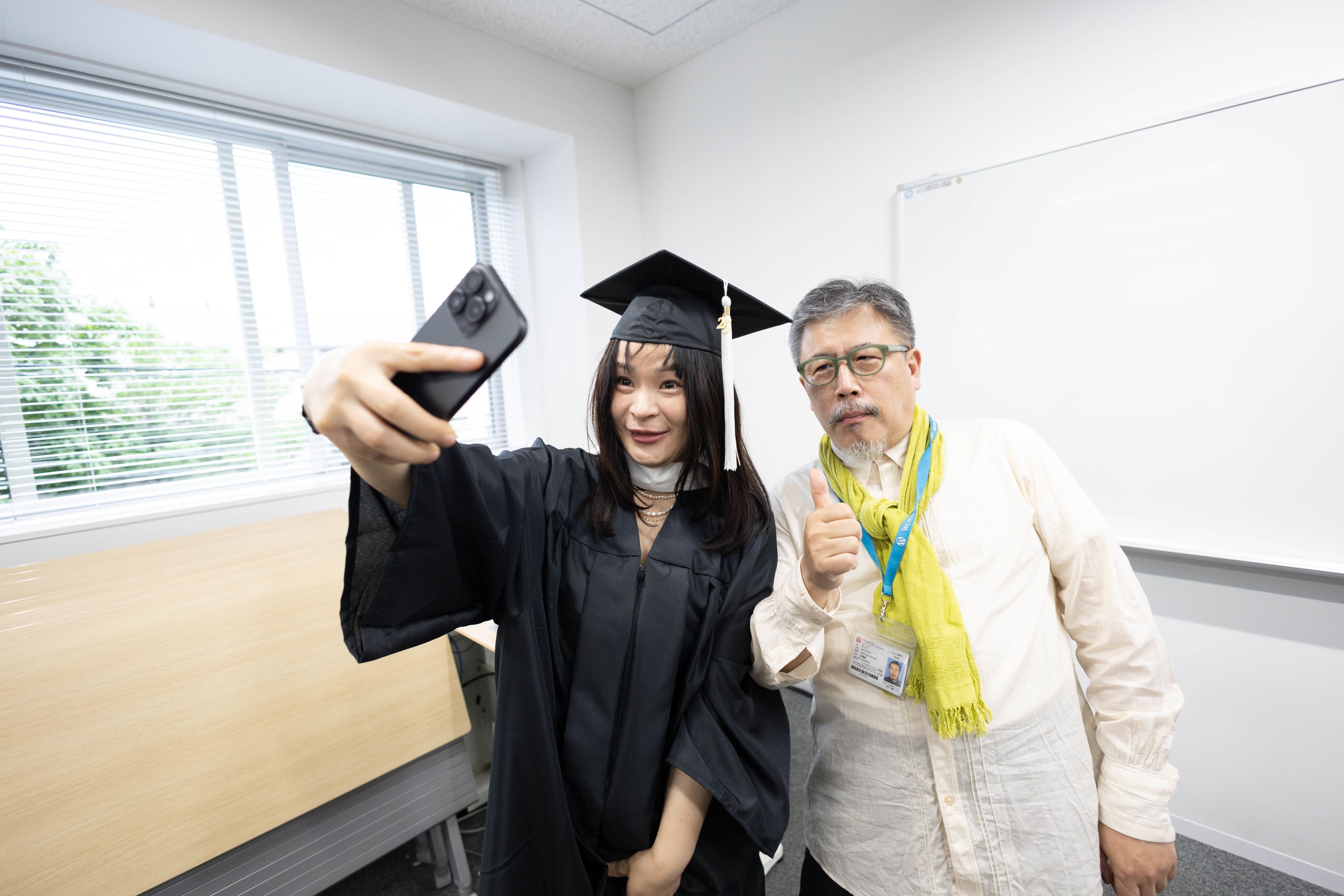 A joyful graduate takes a selfie with a faculty member to celebrate the special moment of commencement.