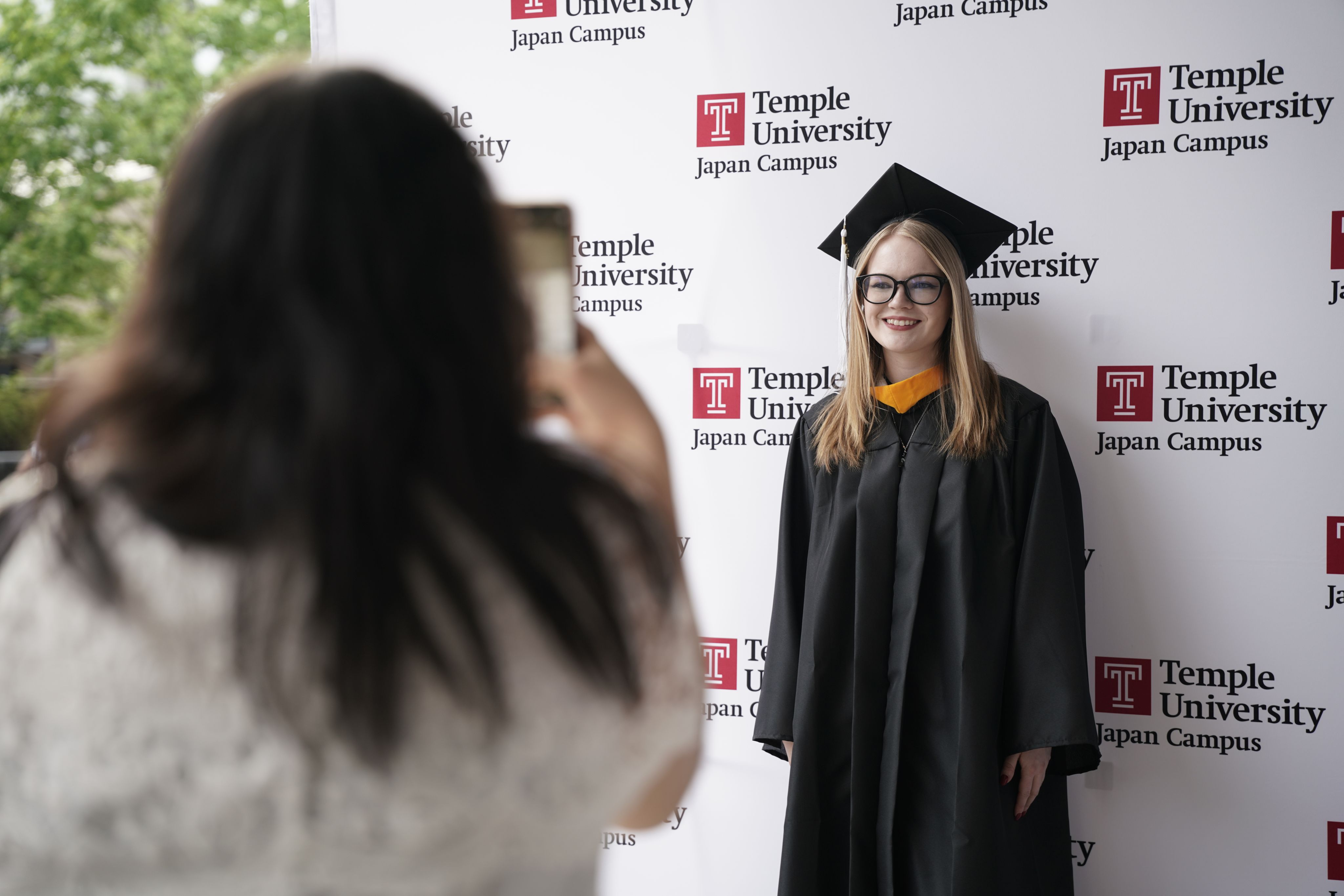 A graduate taking a picture with a TUJ backdrop in front of the Hitomi Hall